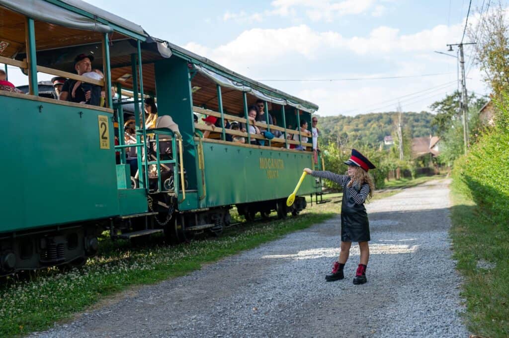 Fetiță salutând turiștii din trenul turistic Mocănița Sovata, cu gesturi de conductor